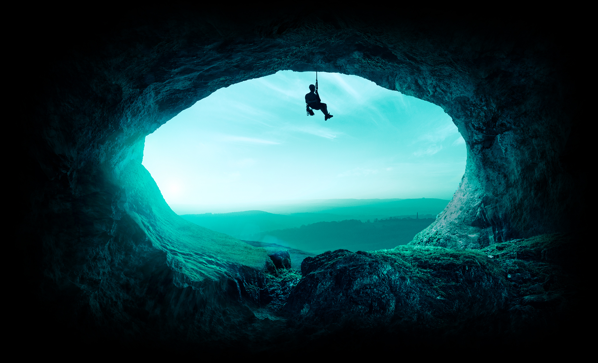Image of a climber swinging from a mouth of a cave